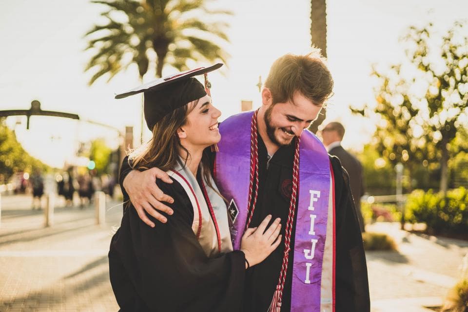 Two graduates in cap and gown outdoors after the ceremony.